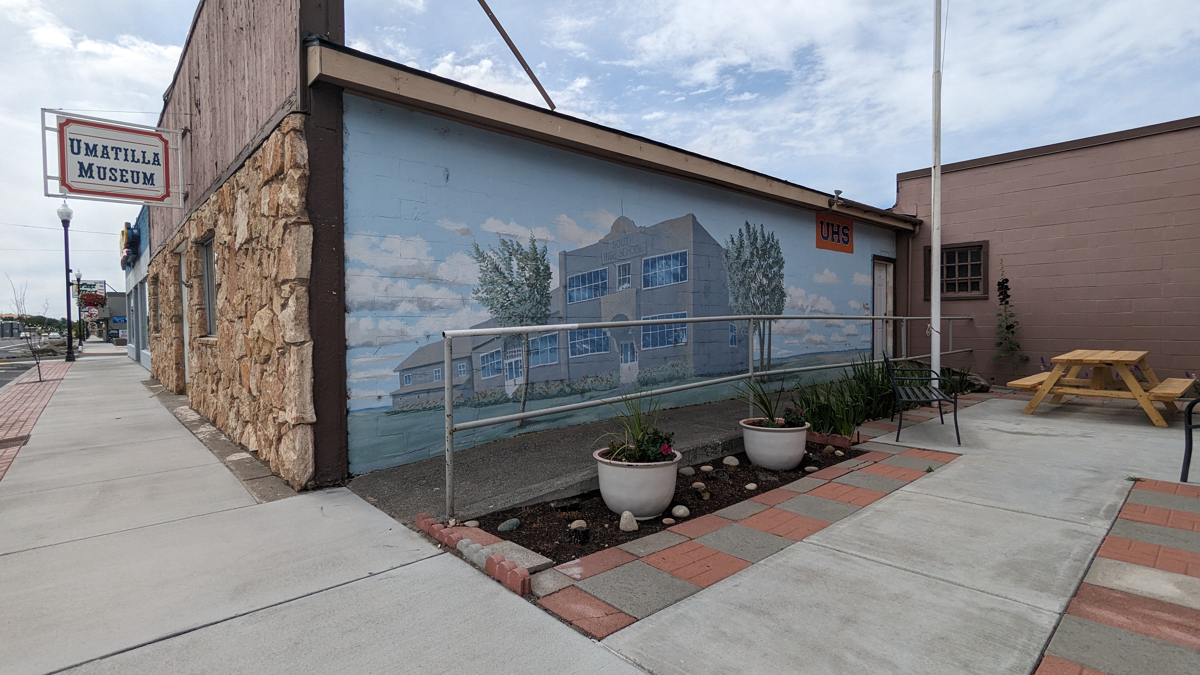 Ramp entrance on side of building overlooking nice courtyard with picnic bench and flowers.